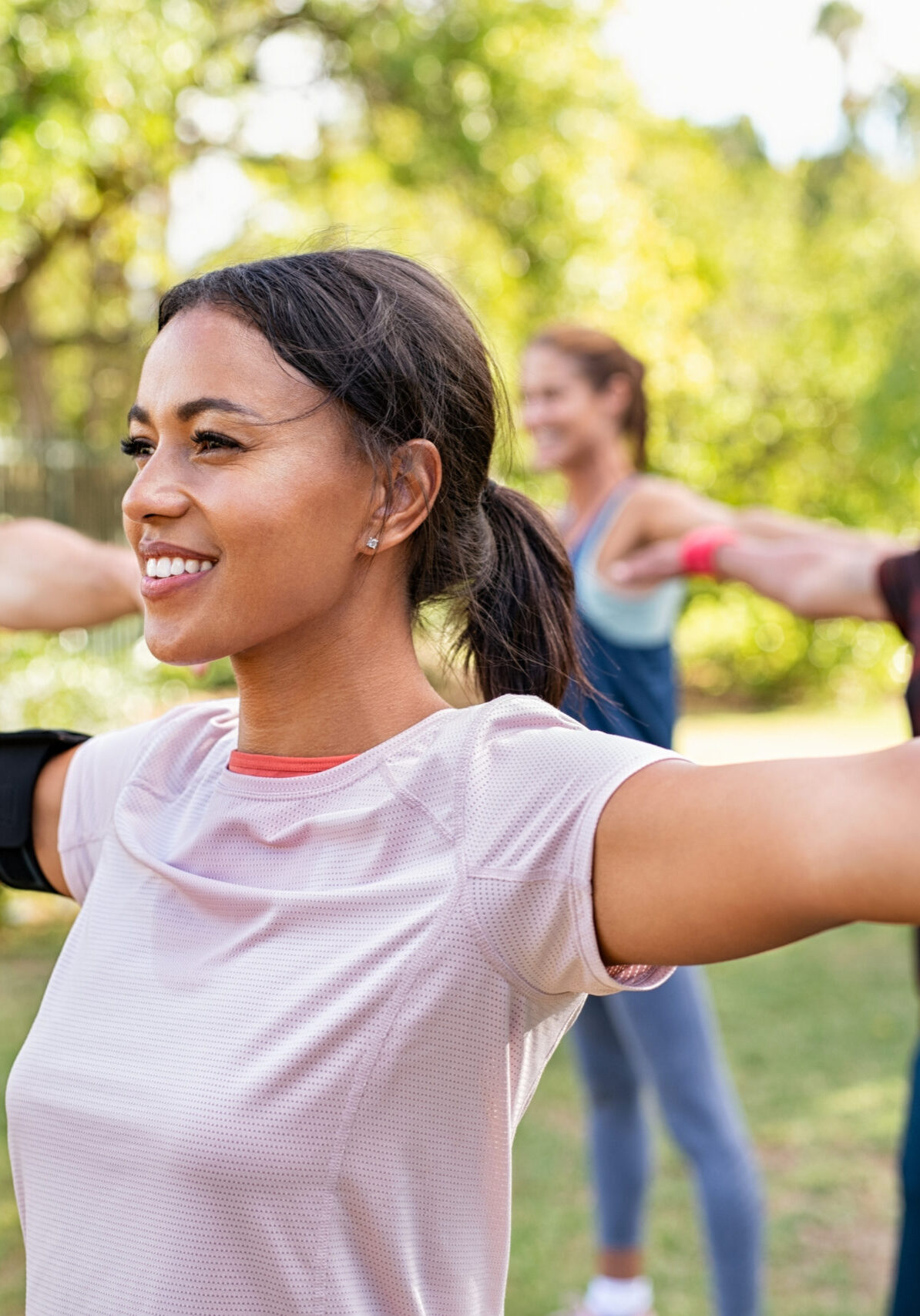 Group of multiethnic mature people stretching arms outdoor. Middle aged yoga class doing breathing exercise at park. Beautifil women and fit men doing breath exercise together with outstretched arms.